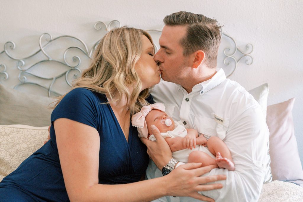 Parents kiss while cradling baby 
