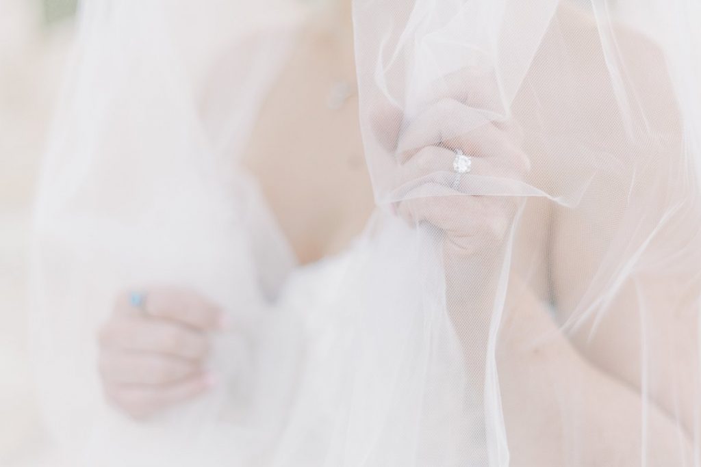 Bride holding up engagement ring under wedding veil