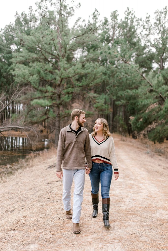 engagement photo with bride and groom walking in pine trees