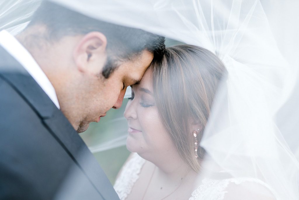 Bride and Groom under brides veil with foreheads touching