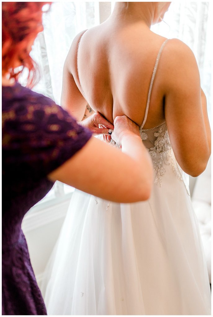 Mother buttoning up bride's wedding gown