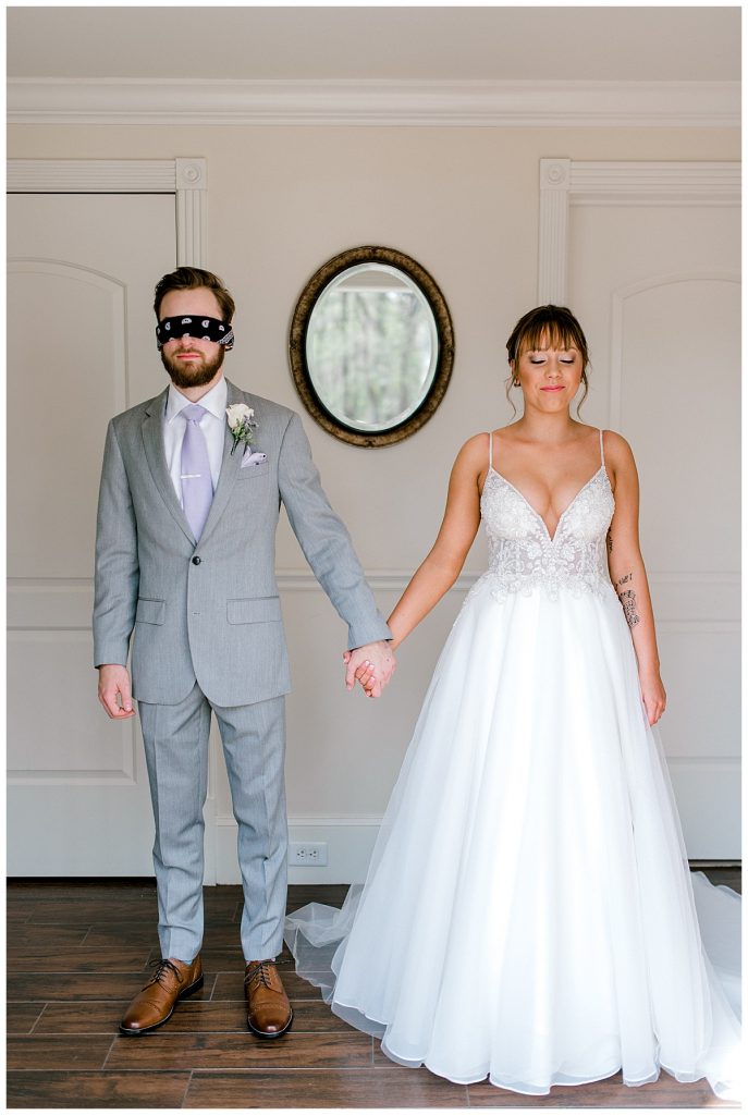 Blindfolded groom holds hands with bride before first look