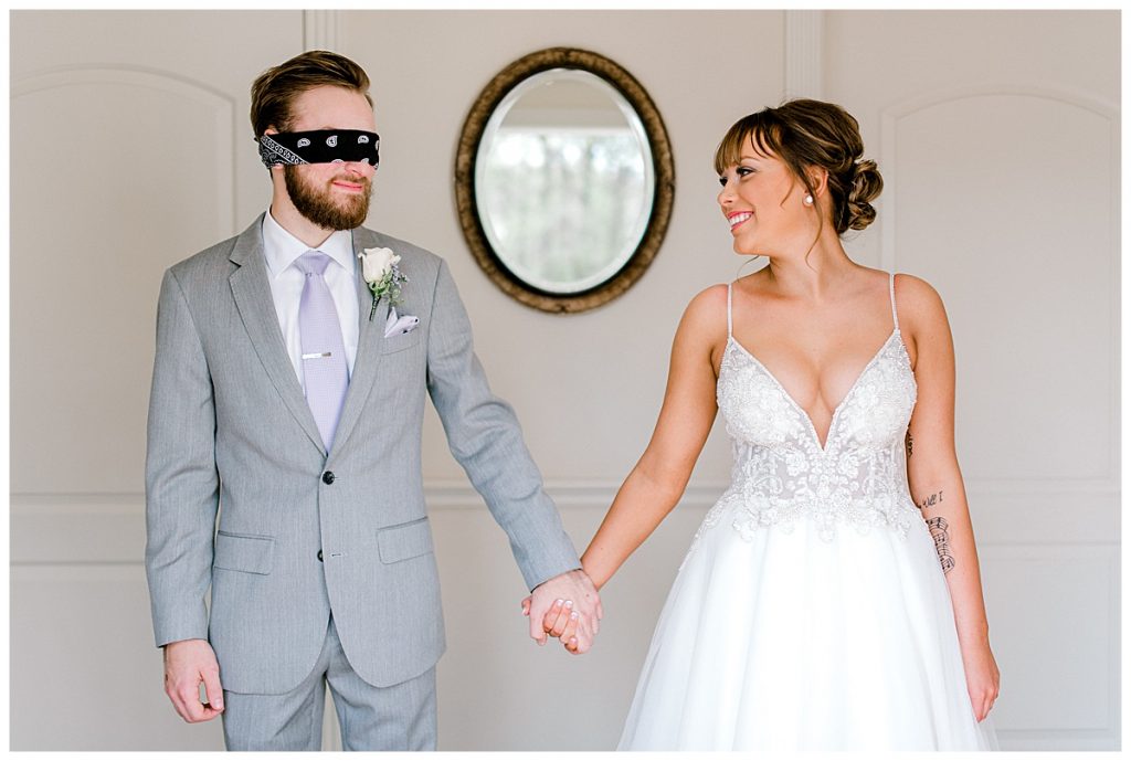 Bride holding hands looking at blindfolded groom| first look