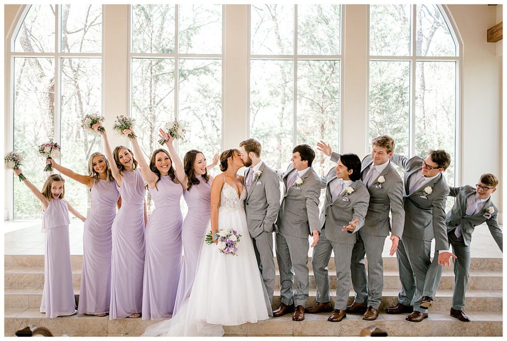 Bridesmaids and groomsmen cheer while bride and groom kiss