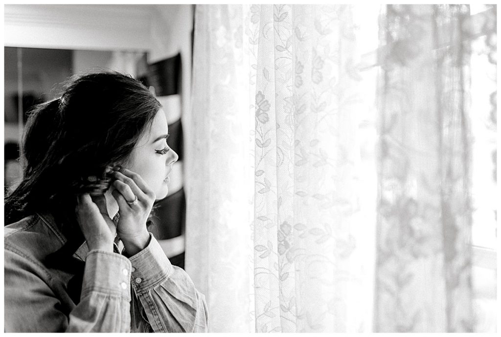 BW bride standing in front of window putting in earrings