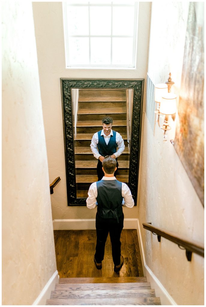 Groom standing in front of mirror at bottom of staircase
