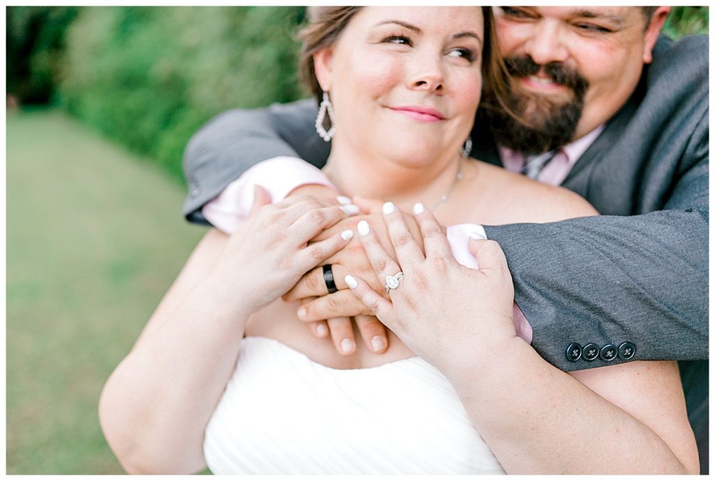 Groom hugging bride from behind showing off wedding rings