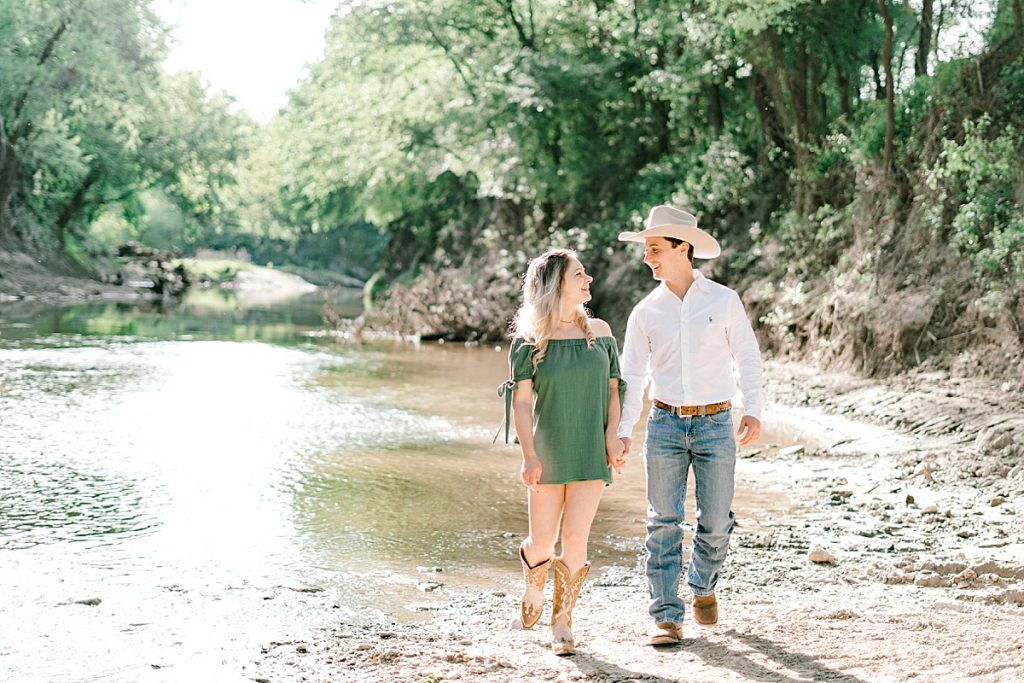 Guy and girl walking in sunlight along creekbed | Hamilton/Hico Engagement 