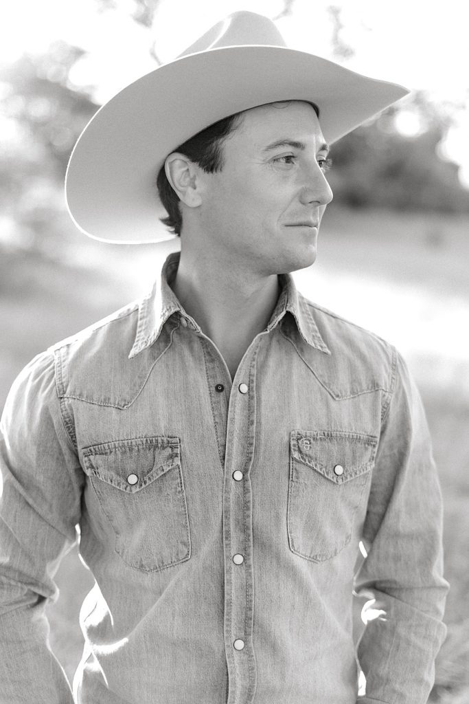 Black and white of guy standing and smiling in cowboy hat