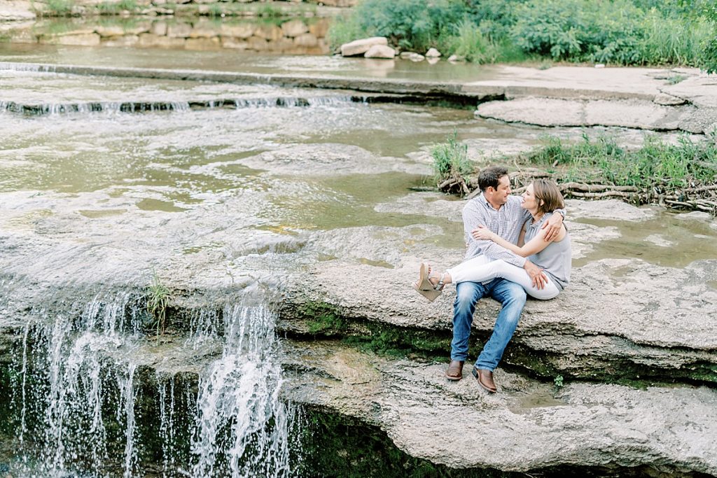 Couple cuddling on rocky falls during their Airfield Falls Engagement Session 