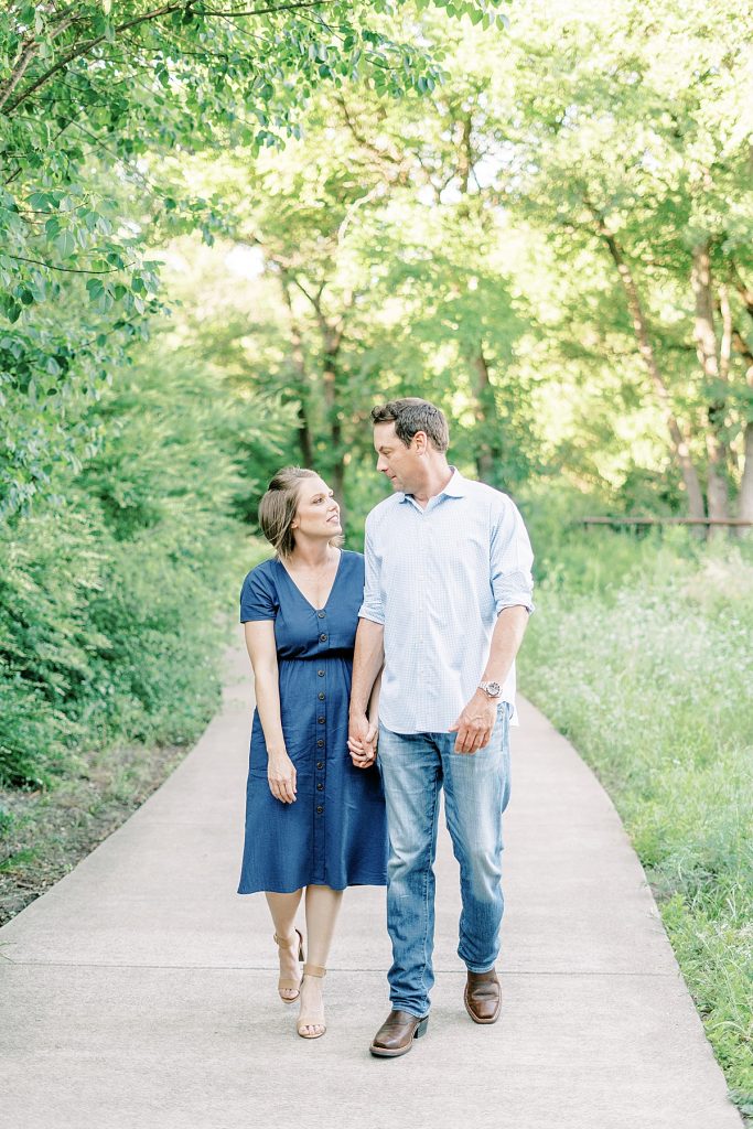 Couple holding hands walking on tree-lined path during their Airfield Falls Engagement Session 