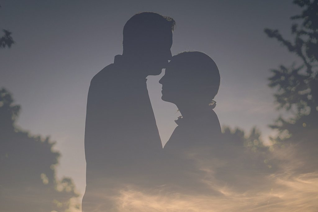 Silhouette in the sky of man kissing woman's forehead at this Airfield Falls Engagement Session 