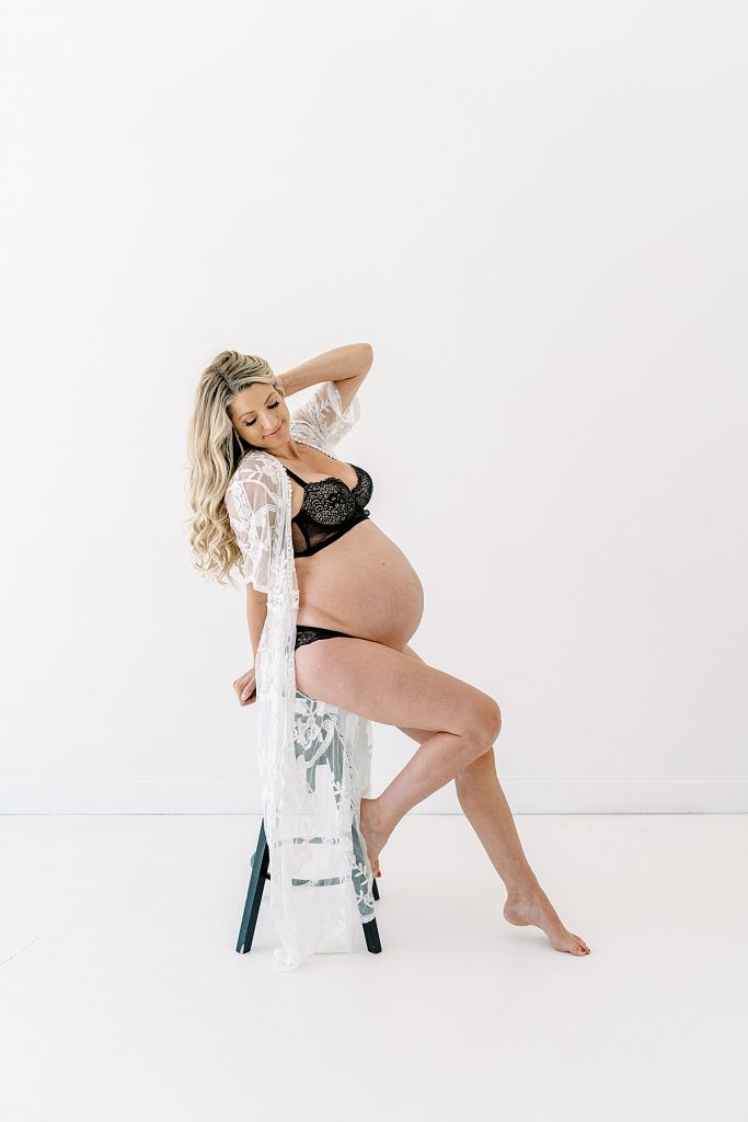 Pregnant woman in lingerie sitting on stool in Lumen Room maternity session