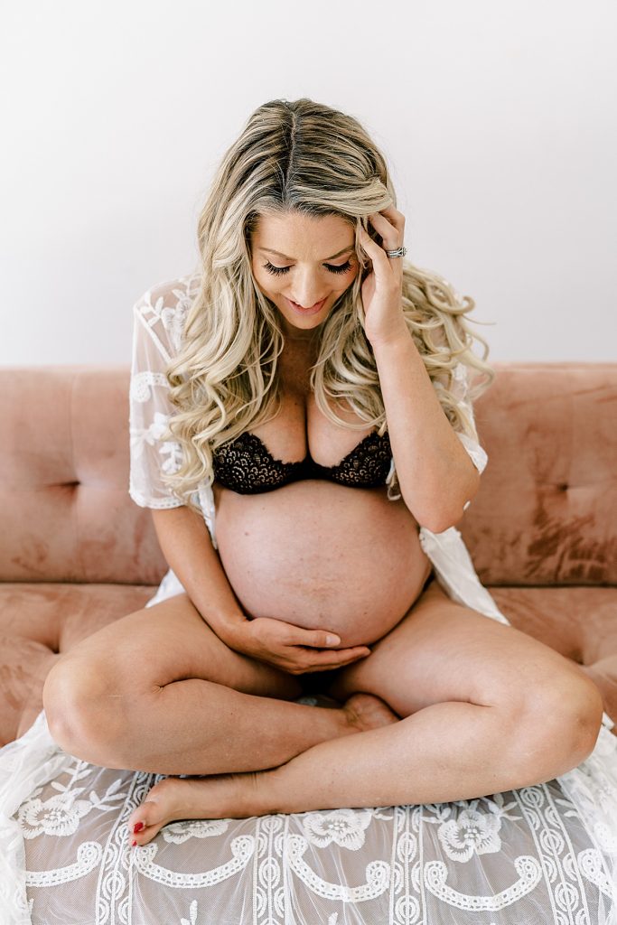 Woman sitting in lingerie on couch holding pregnant belly