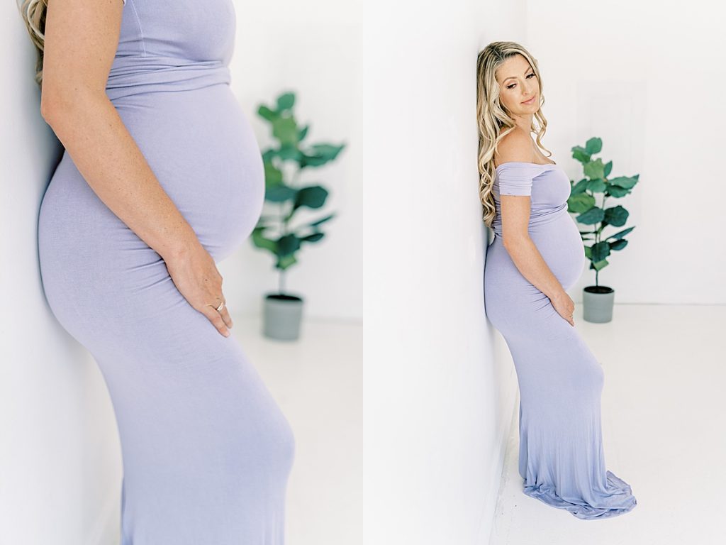 pregnant woman in long dress leans against wall in Lumen Room maternity