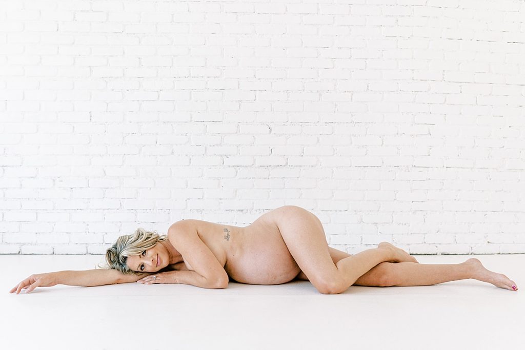 Nude blonde pregnant woman laying on floor in Lumen Room maternity session
