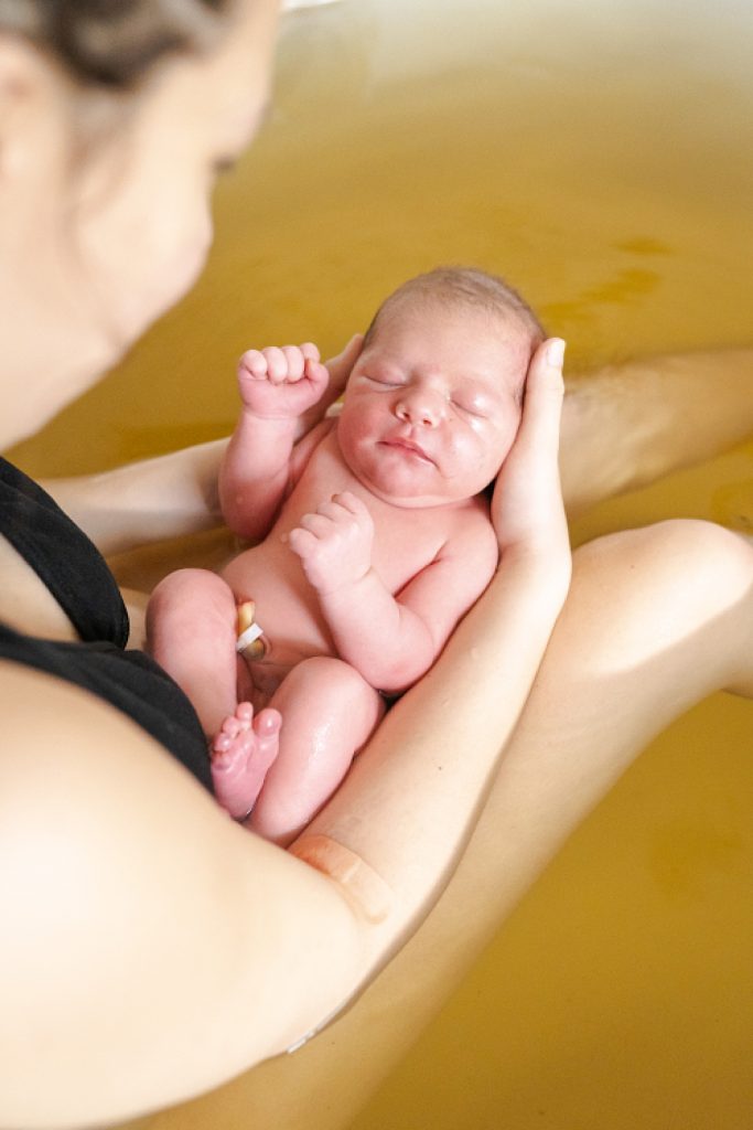 Mother holding newborn baby in healing bath