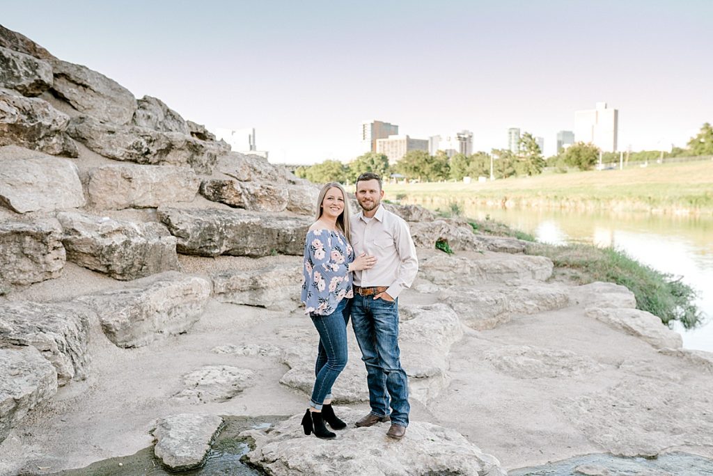 Couple standing on rocks with city skyline in Fort Worth engagement session