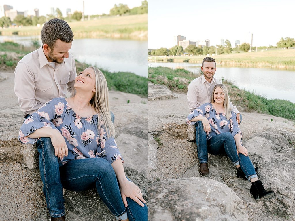 Engaged couple sitting on rocks with city skyline in Trinity Park Fort Worth engagement