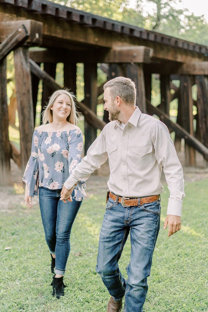 Guy leading girl through field in Fort Worth stockyard engagement