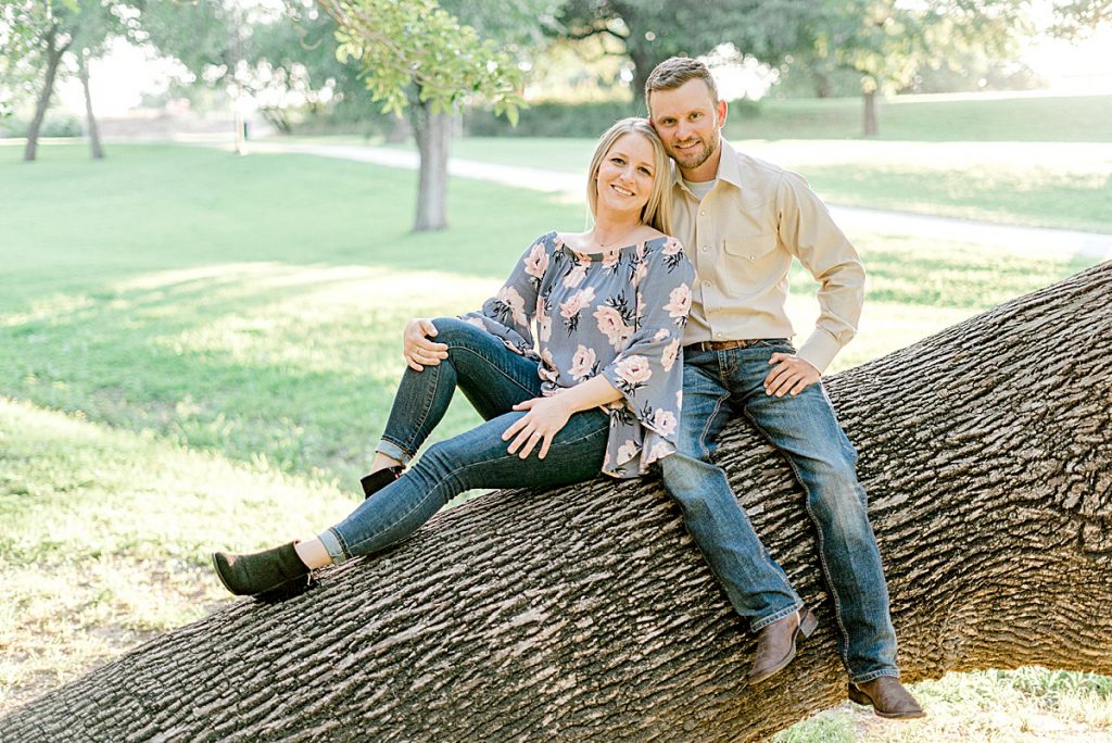 Engaged couple sitting on huge tree in Fort Worth Trinity Park engagement