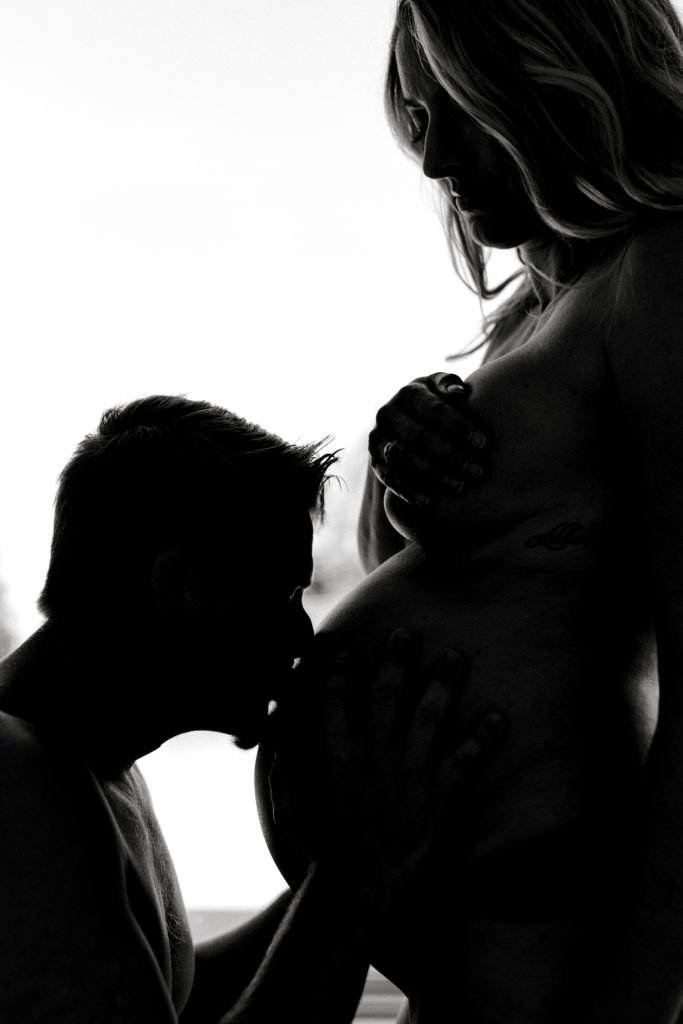 BW silhouette husband kneeling kissing wife's pregnant belly