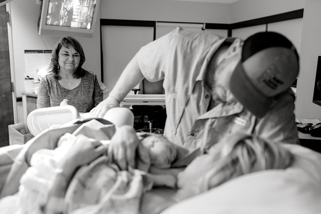 BW mother smiling while parents swoon over newborn