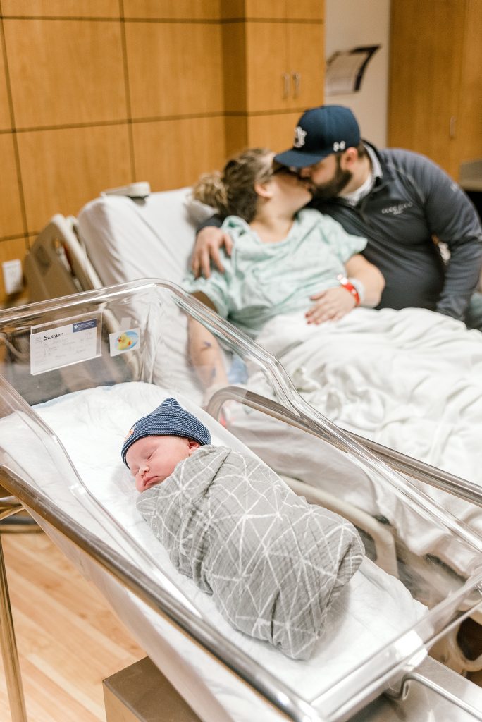 Baby in bassinet while parents kiss in background| Baylor Scott & White Birth 
