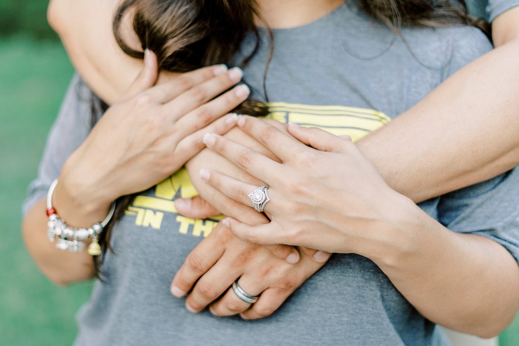 Guy wraps arms around girl showing off round diamond engagement ring