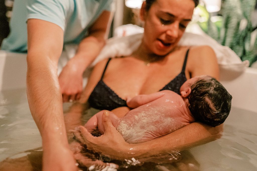 Couple holding new baby in bathtub after water delivery
