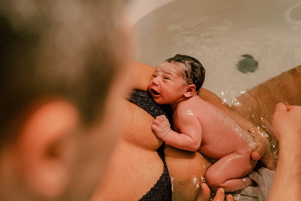 Couple holding new baby in bathtub after water delivery