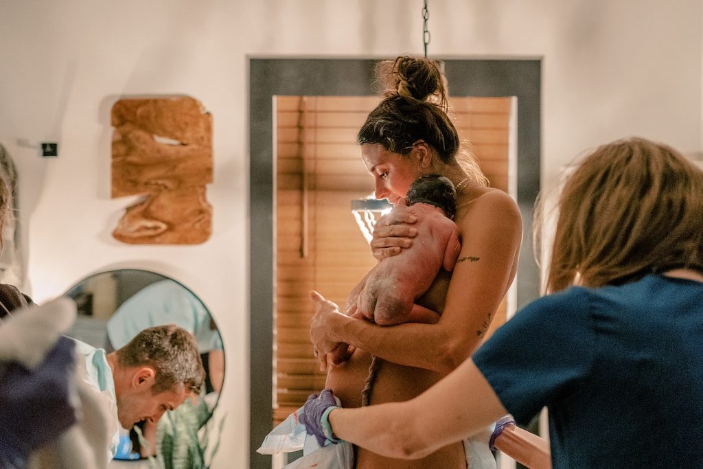 Mother holding newborn while nurse cleans her up