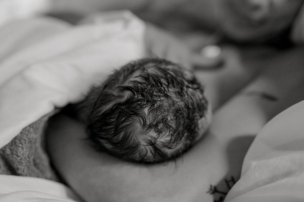 Newborn with head of hair being cradled after an Origins water birth 