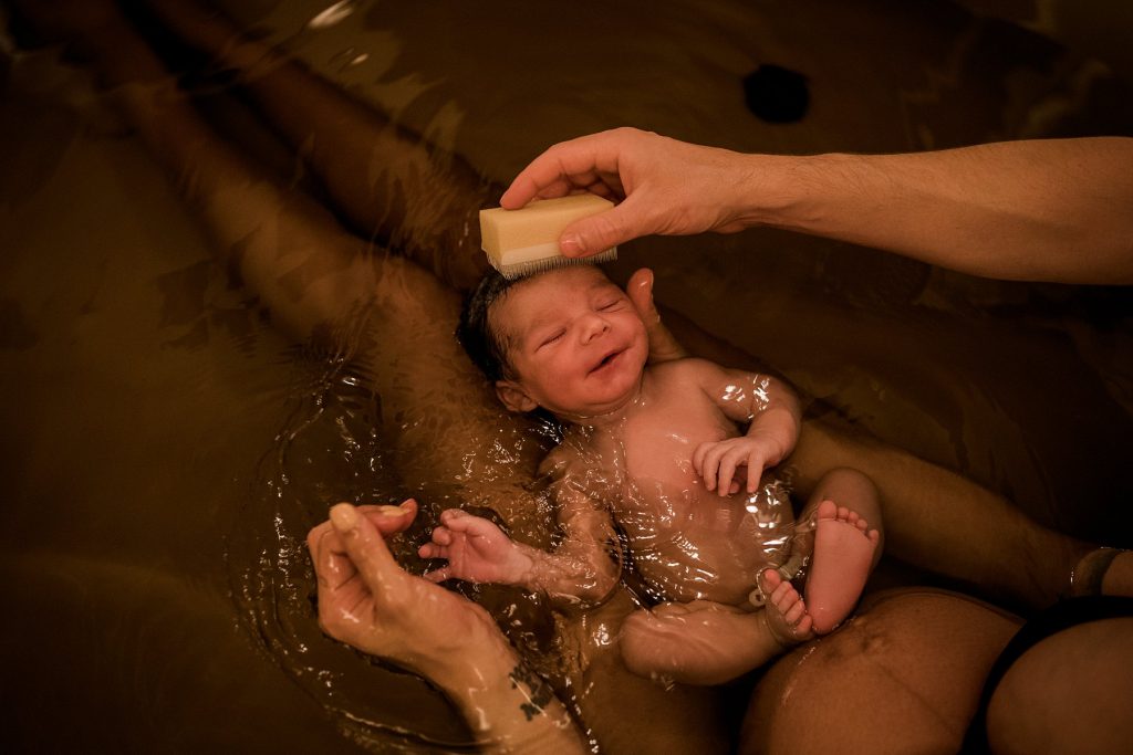 Baby being held in moms lap in bathtub after Origins water birth