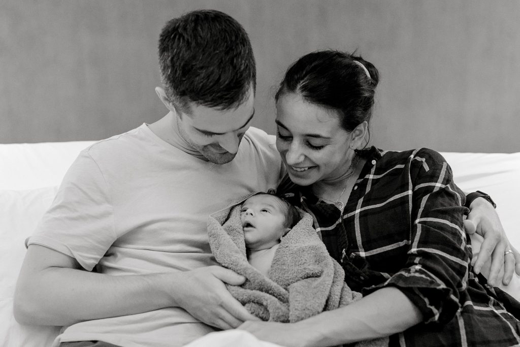 BW couple in bed cuddling their newborn baby