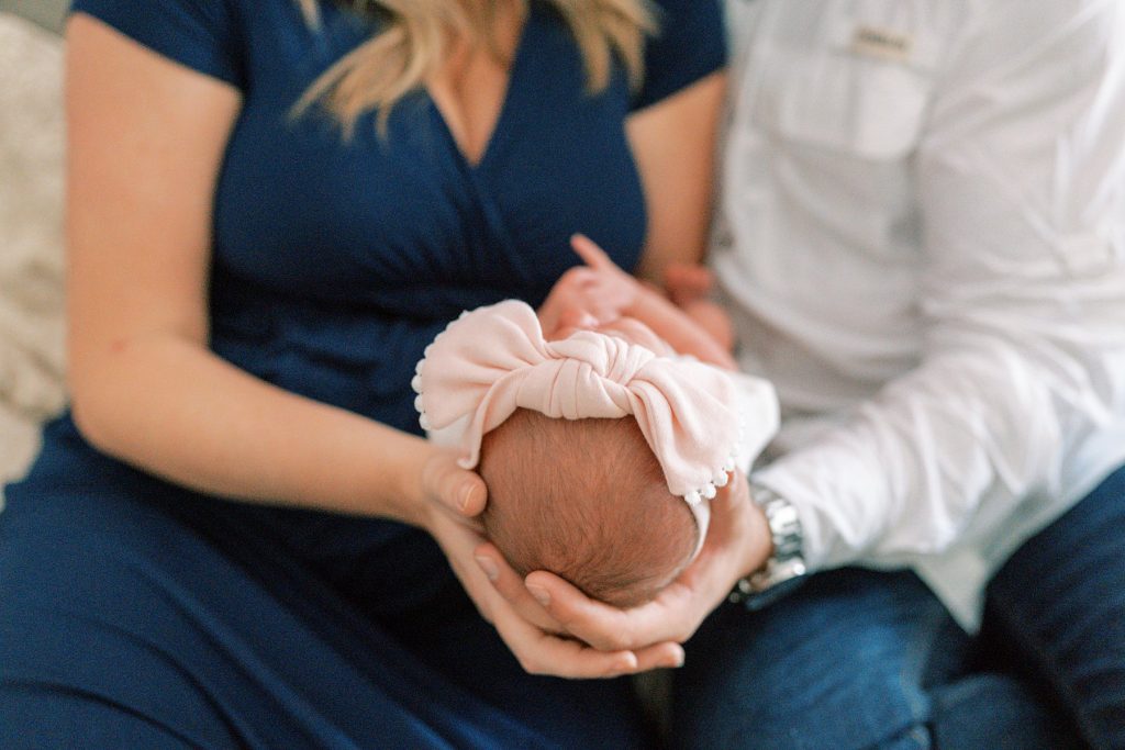 Parents holding newborn head with bow on it during their lifestyle newborn session 