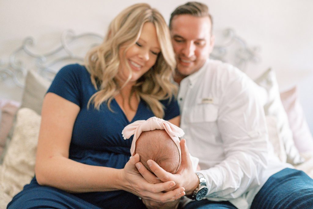 Parents holding newborn head with bow on it during their lifestyle newborn session 