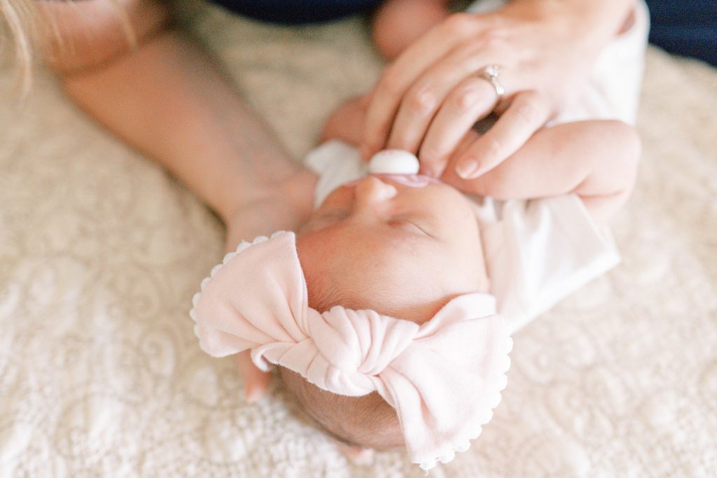 Newborn baby in mothers hands on bed with big pink bow