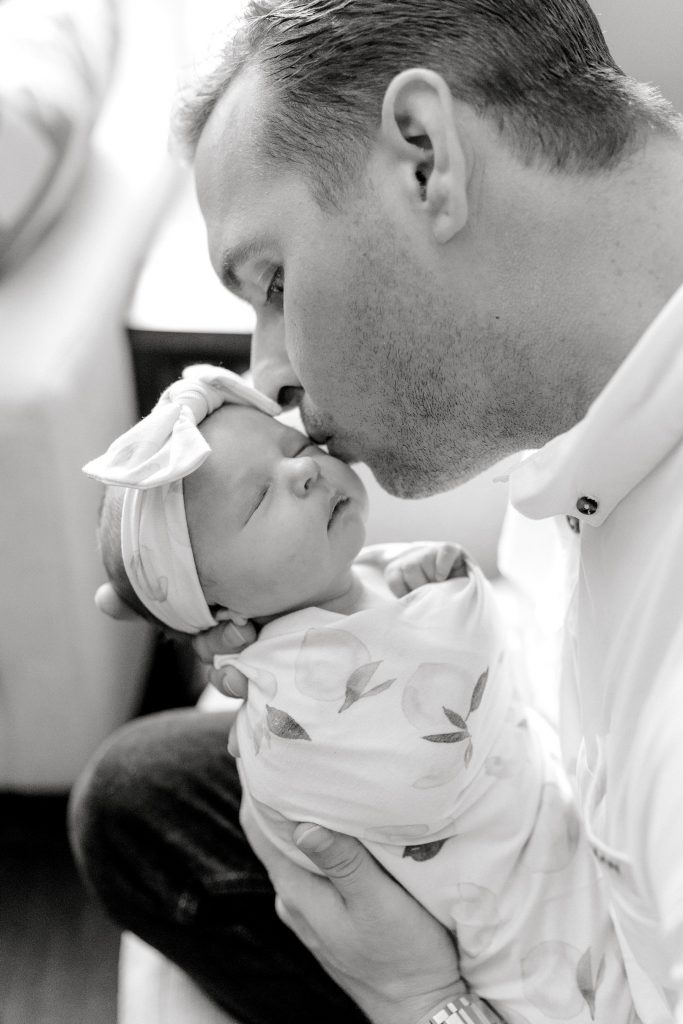 BW of father holding newborn baby girl kissing her cheek