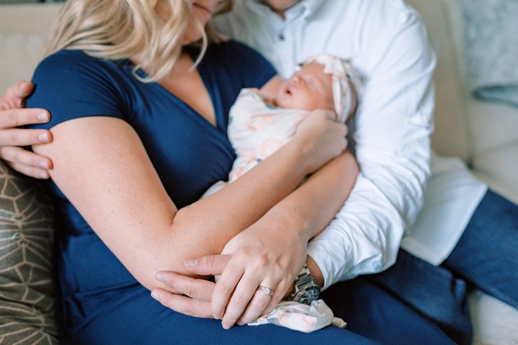 Parents cradling newborn baby girl and holding hands