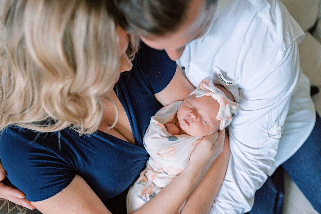 Parents cradling newborn baby girl looking down at her during her lifestyle newborn session 