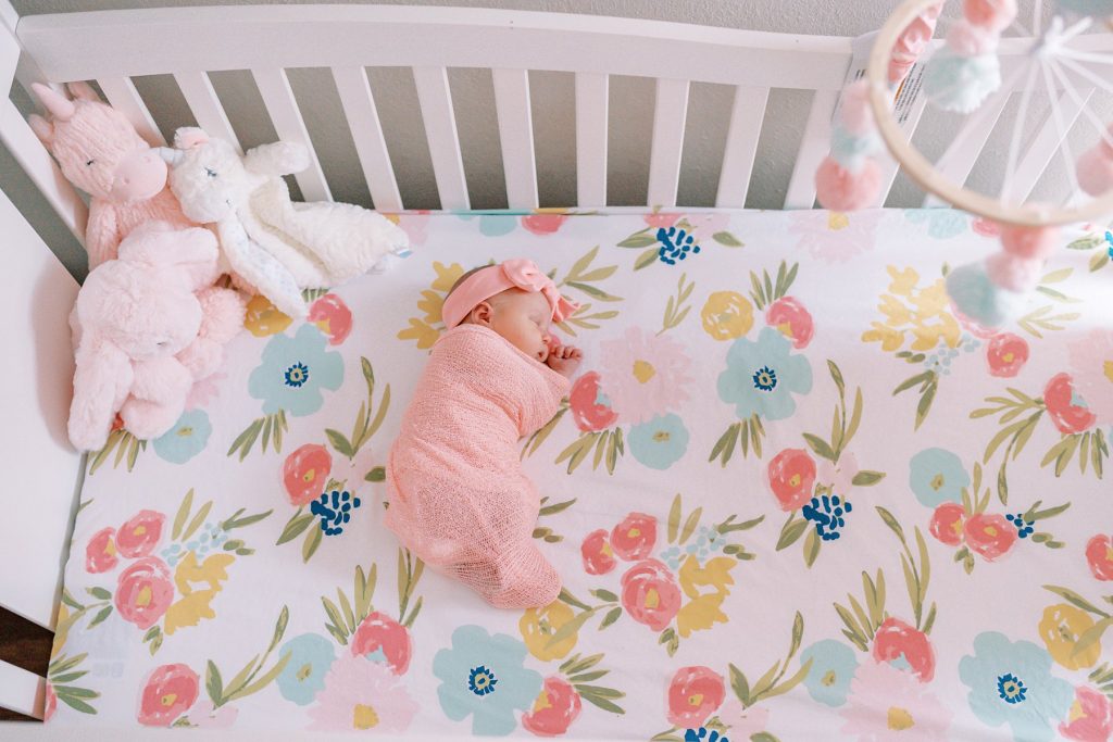 Newborn baby girl wrapped in pink blanket laying in crib
