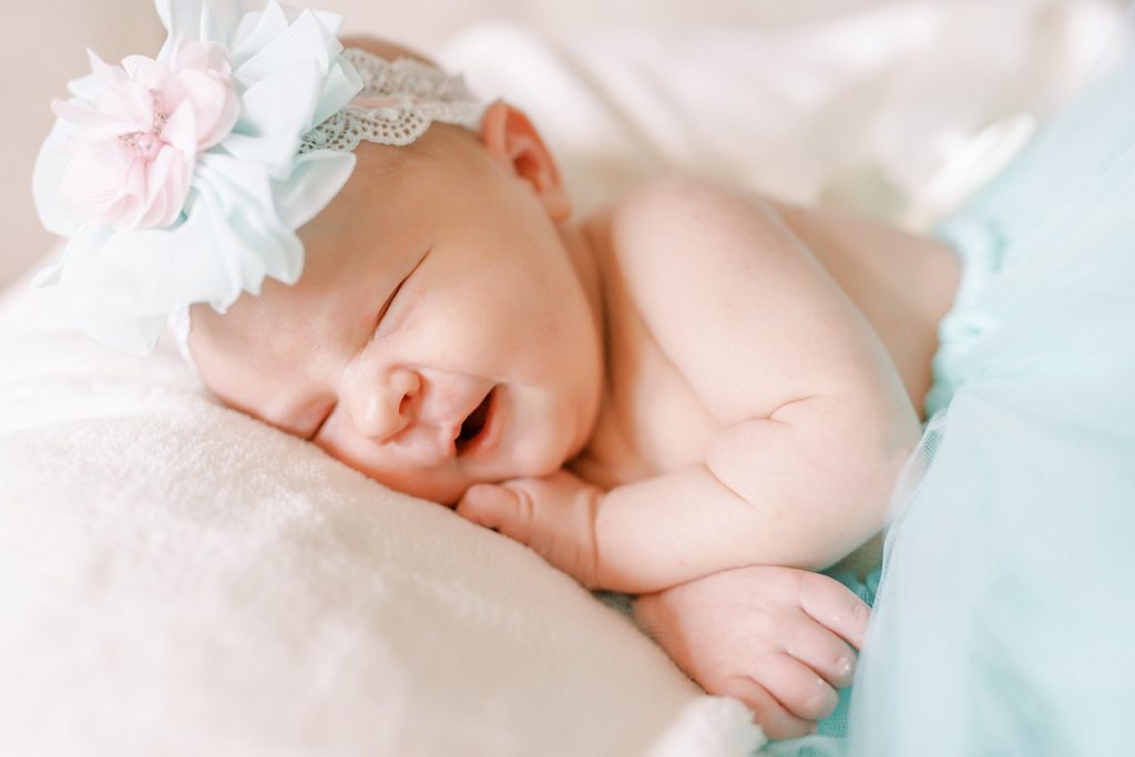 Newborn baby girl in teal tutu and bow laying grinning on soft blanket during her lifestyle newborn session 