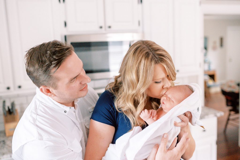 Parents kissing freshly bathed baby in towel during her lifestyle newborn session 