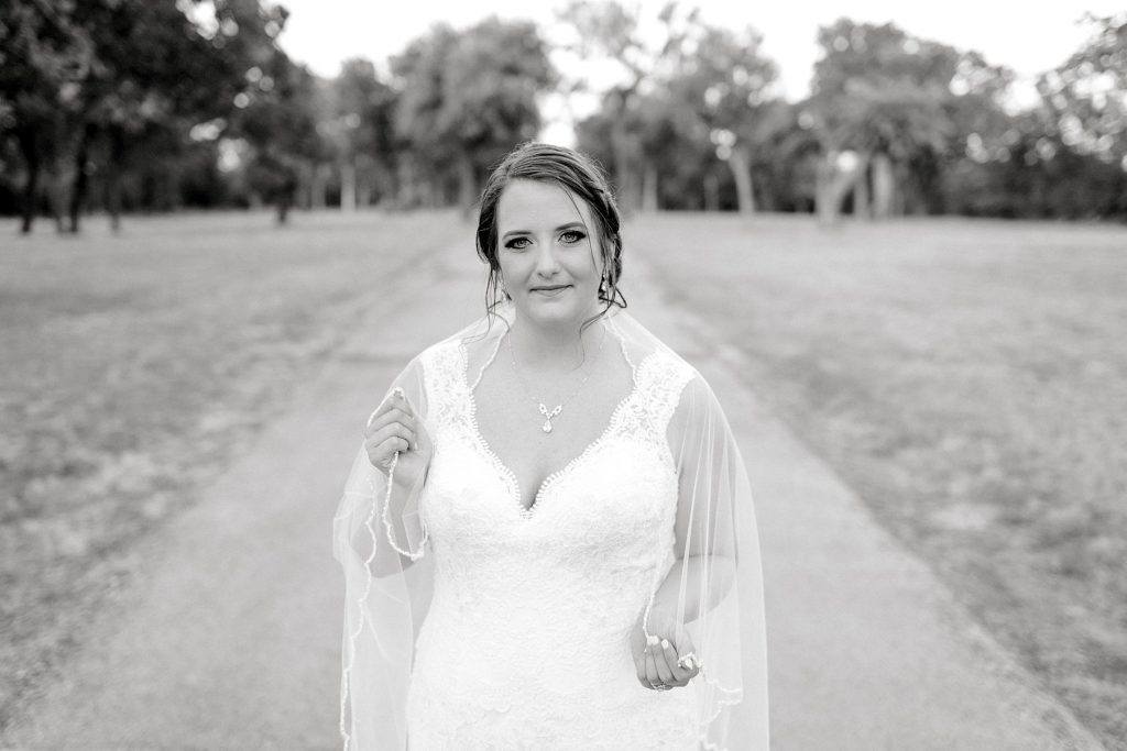 BW bride standing in wedding gown and holding edge of veil in middle of road at Wildcatter Ranch bridal session