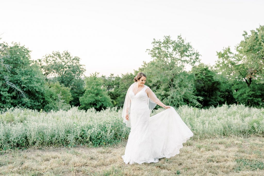 Bride looking down holding wedding gown train out in field at Wildcatter Ranch Texas bridal session