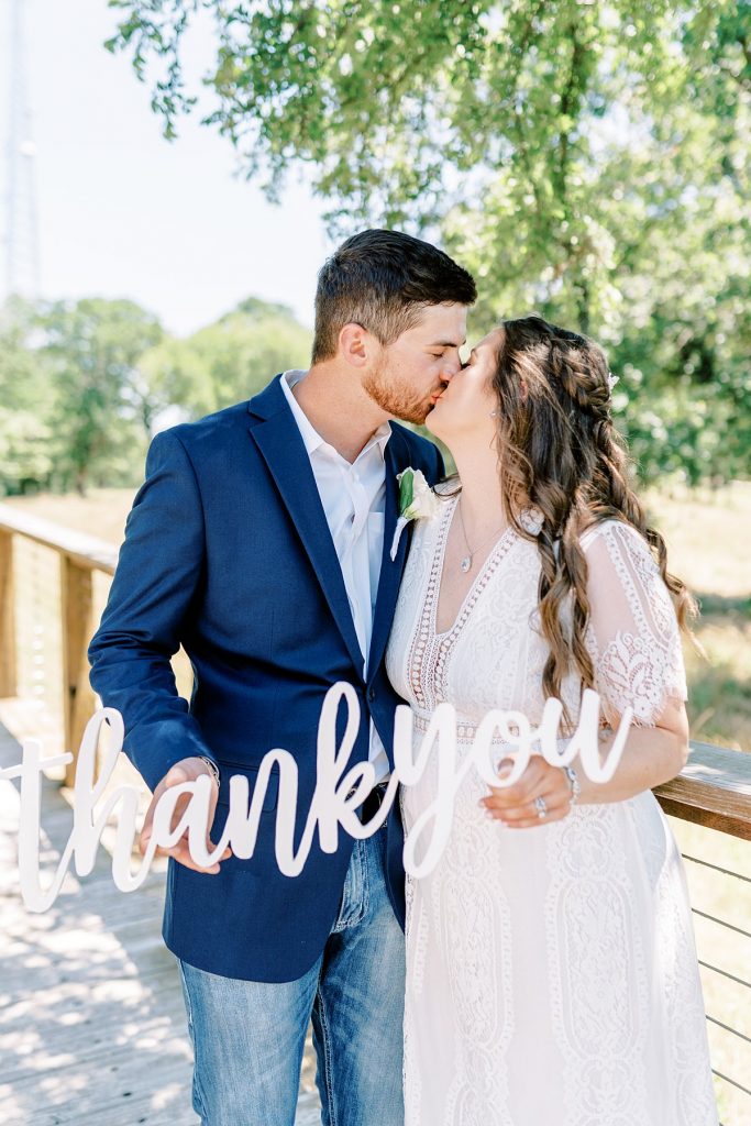 Bride and groom kiss while holding 'thank you' sign at Texas elopement