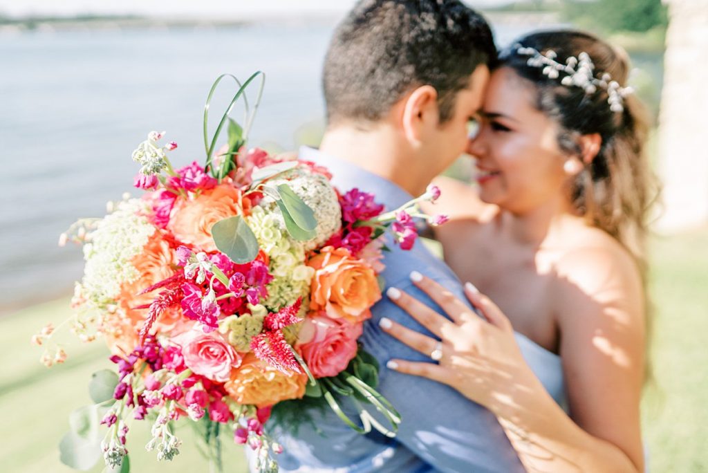 Bride and groom nuzzling showing off pink and orange wedding bouquet at Lake Granbury elopement