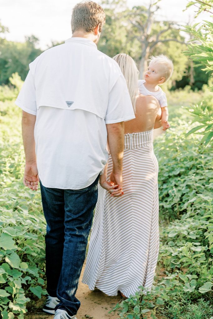 Couple holding hands walking through greenery holding baby