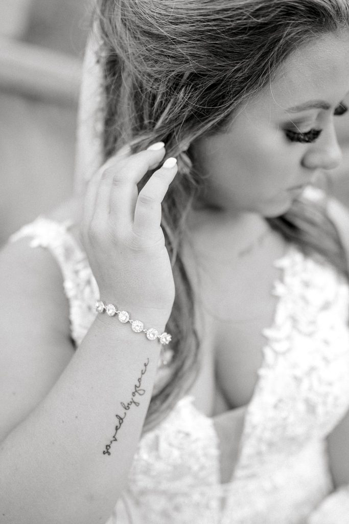 BW bride reaching up to touch hair showing bridal jewelry